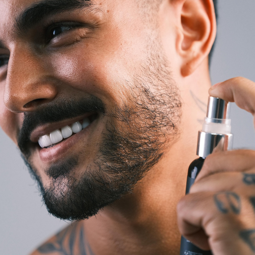 Homem sorrindo aplicando o tônico Fórmula X na barba